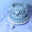 Pastel blue cake with piped ruffles and bows beside a Colour Mill Baby Blue bottle