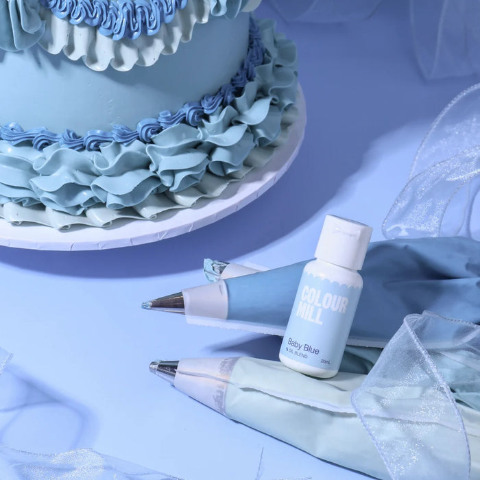 Colour Mill Baby Blue Oil Blend bottle beside blue icing piping bags and a decorated cake