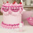 Pastel pink cake with piped pink decorations and cherries beside a Colour Mill Baby Pink bottle
