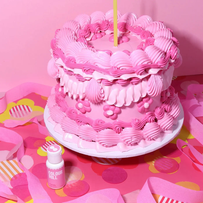 Pink cake with piped ruffles and flowers beside a Colour Mill Candy bottle