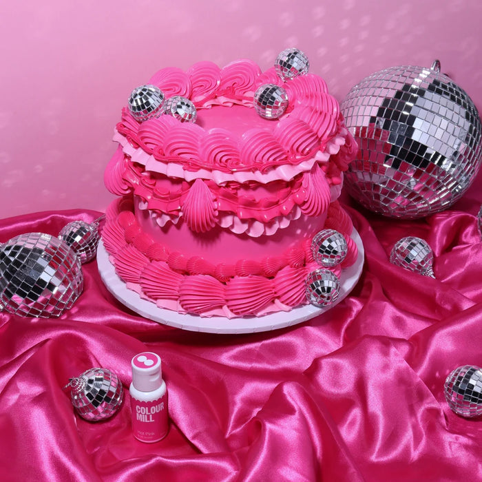 Hot pink cake with piped ruffles and silver disco balls beside a Colour Mill Hot Pink bottle
