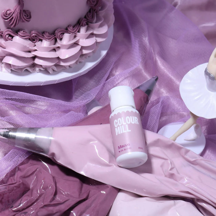 Colour Mill Mauve Oil Blend bottle on mauve icing piping bags beside a decorated cake