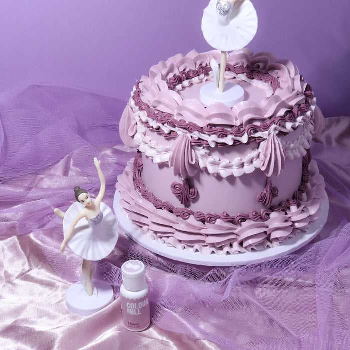 Mauve buttercream cake with piped ruffles and ballerina decorations beside a Colour Mill Mauve bottle
