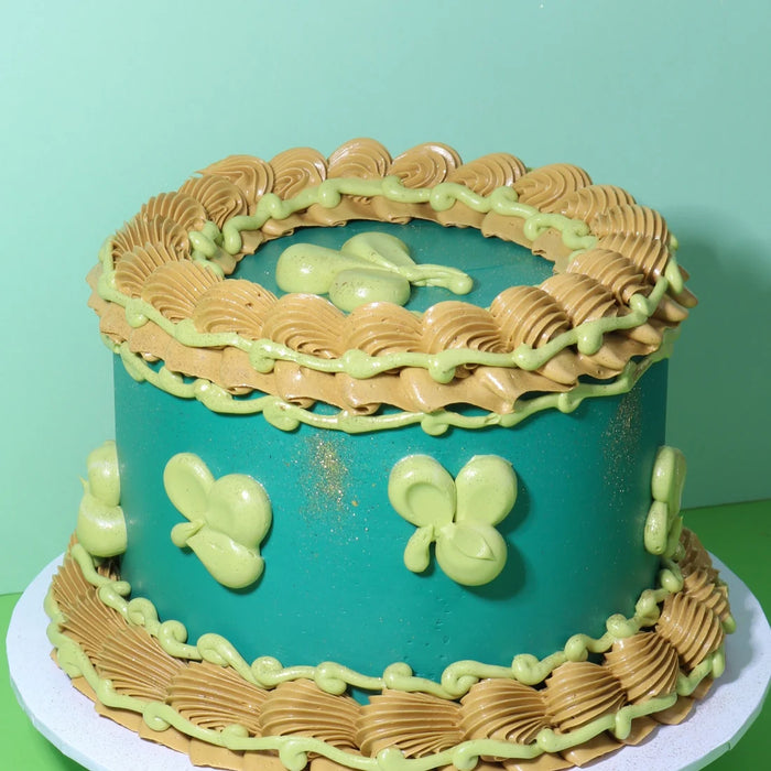 Teal cake with mustard-coloured piped borders and light green butterfly decorations