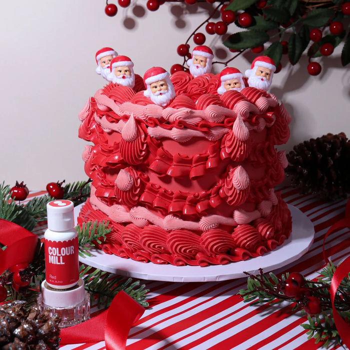 Red and pink piped Christmas cake with Santa decorations beside Colour Mill Red food colour