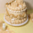Beige and cream piped cake with shell decorations beside Colour Mill Sand food colour