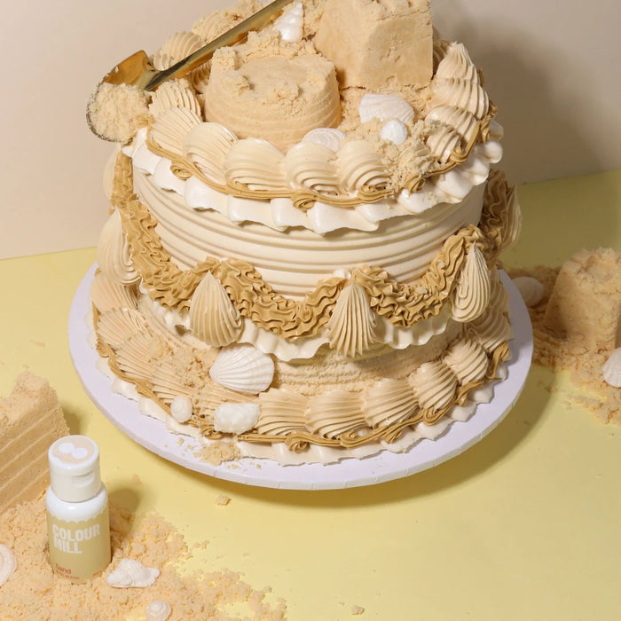 Beige and cream piped cake with shell decorations beside Colour Mill Sand food colour
