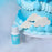 Colour Mill Sky Blue bottle beside blue cake piping and white cloud decorations