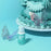 Colour Mill Tiffany bottle beside blue-green cake piping and butterfly decorations