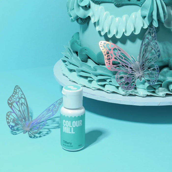 Colour Mill Tiffany bottle beside blue-green cake piping and butterfly decorations