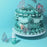 Blue-green piped cake with butterfly decorations beside Colour Mill Tiffany food colour