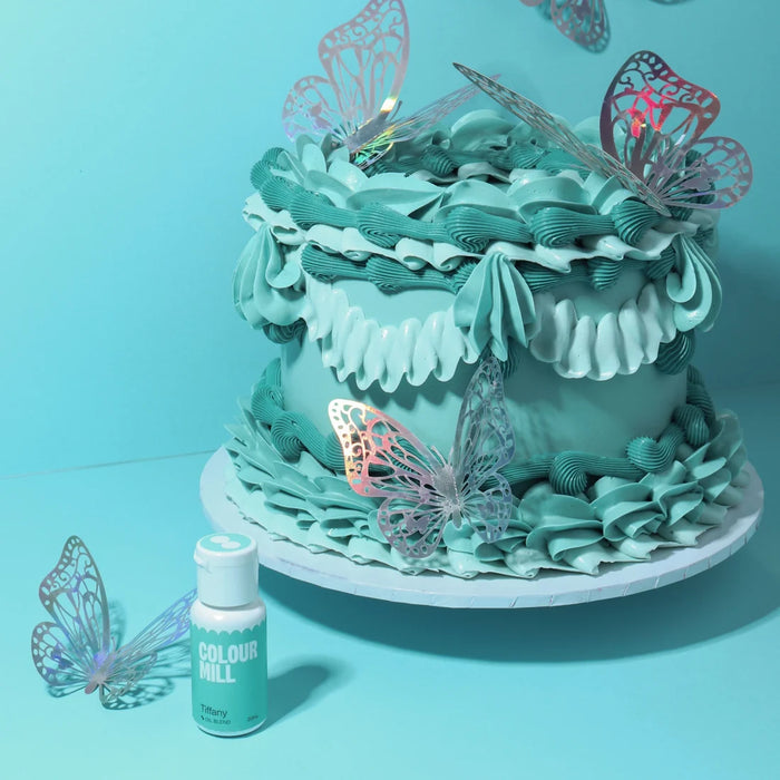 Blue-green piped cake with butterfly decorations beside Colour Mill Tiffany food colour
