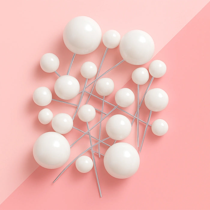 Assorted white ball cake toppers on slender picks against a pink background