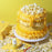 Yellow buttercream cake with piped ruffles and popcorn beside a Colour Mill Yellow bottle