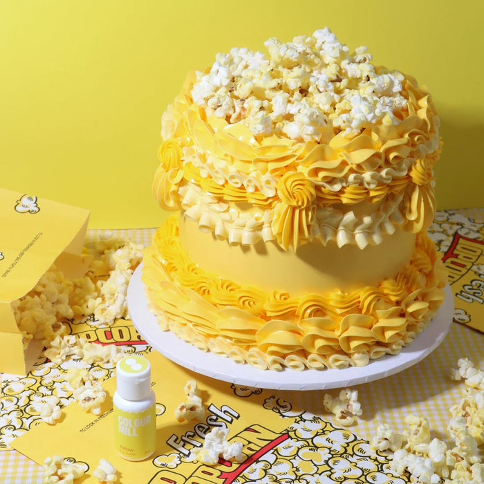 Yellow buttercream cake with piped ruffles and popcorn beside a Colour Mill Yellow bottle